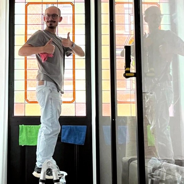 Arne standing on a ladder  smiling with thumbs up after installation of a stained glass window.