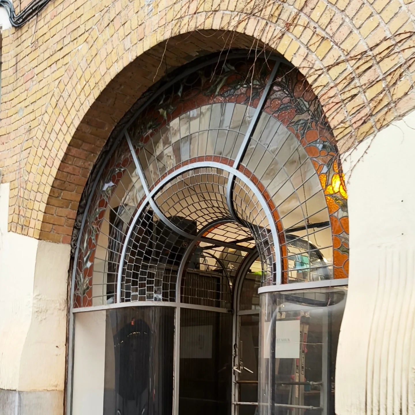 Curved stained glass shop front in transparant glass with floral motives in ambers and greens. Restored by studio bxlart.