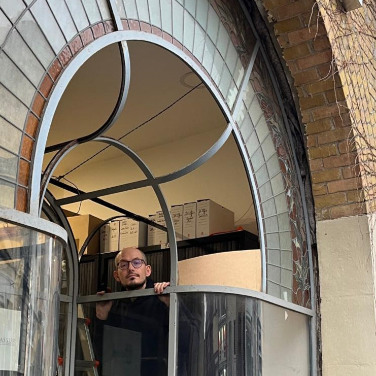 Arne looking through the opening of a curved stained glass shop front in transparant glass and  with floral motives in ambers and greens.